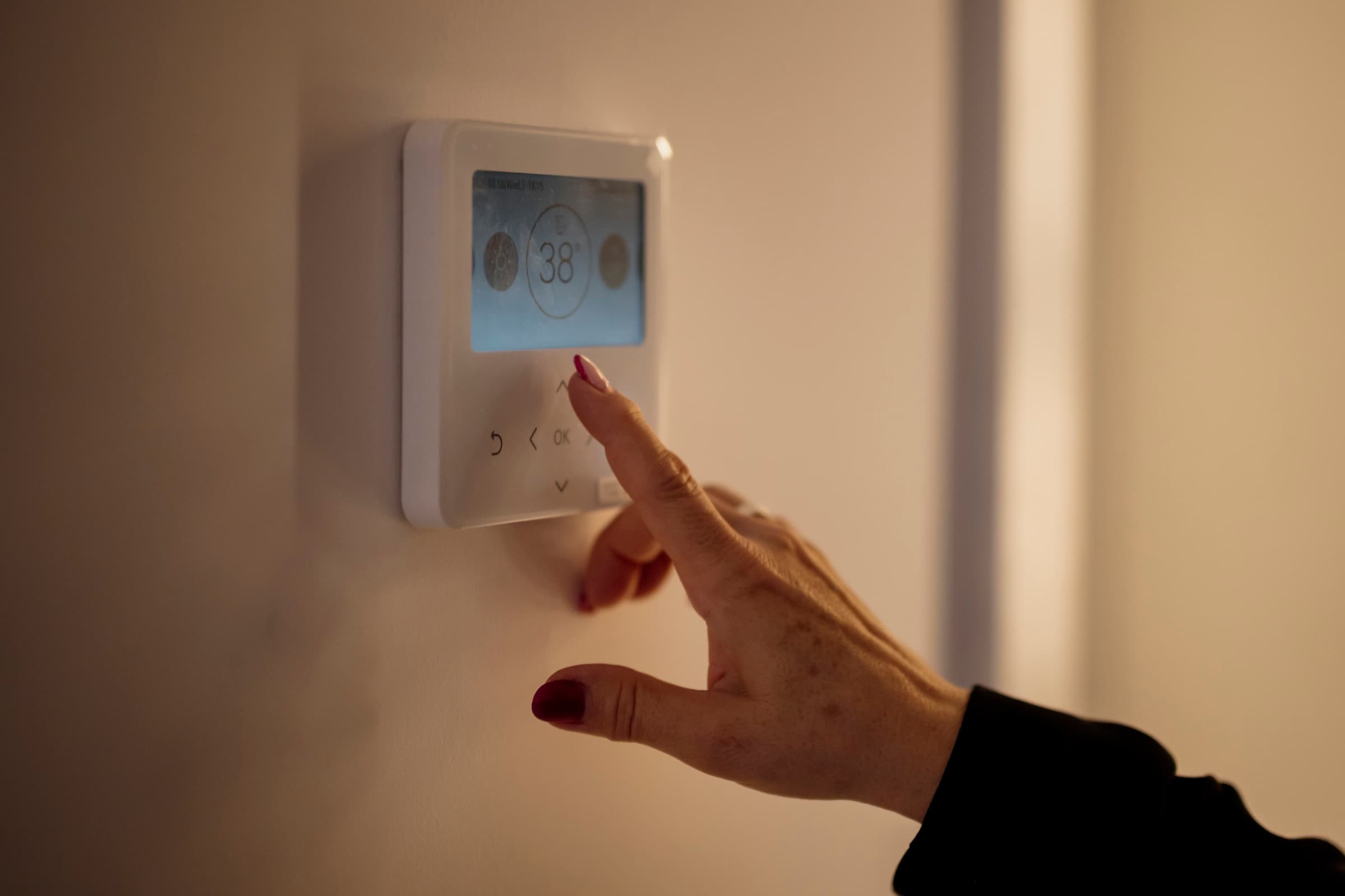 A hand adjusting a modern digital wall thermostat.