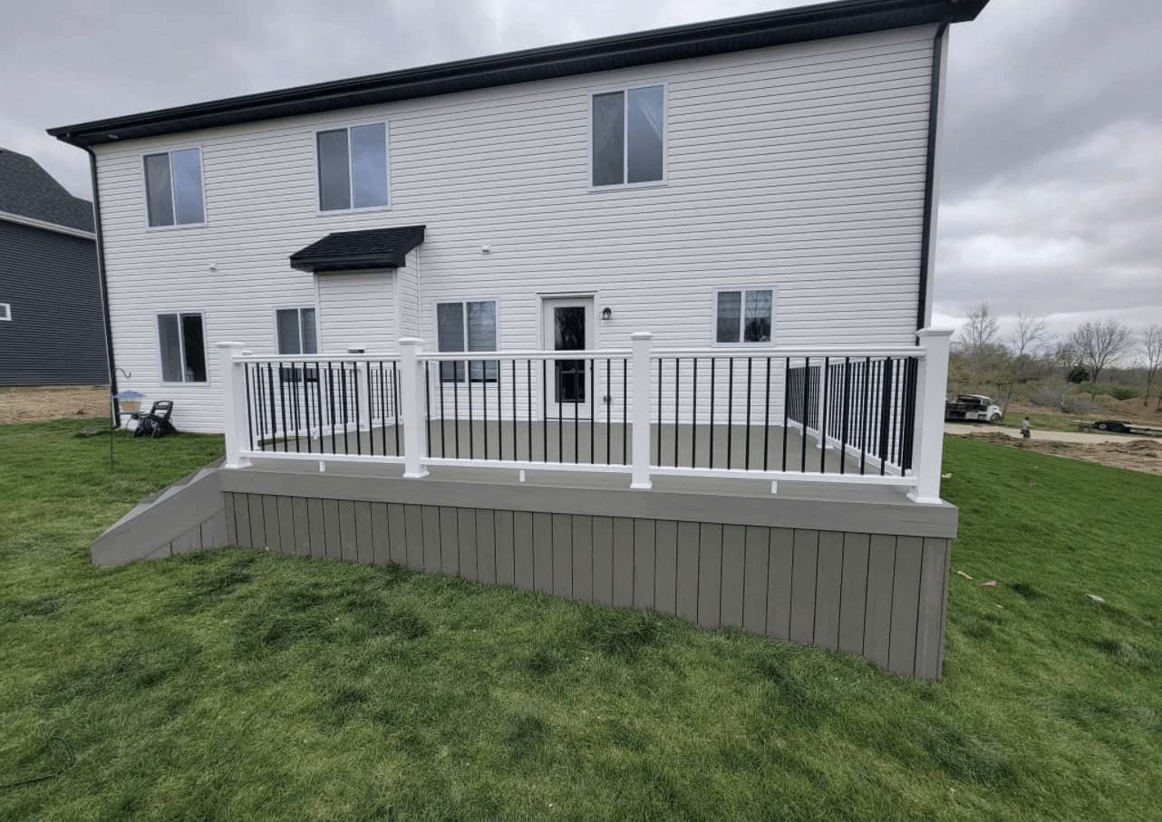 A completed composite deck across the back of a house with white railings and stairs to the yard